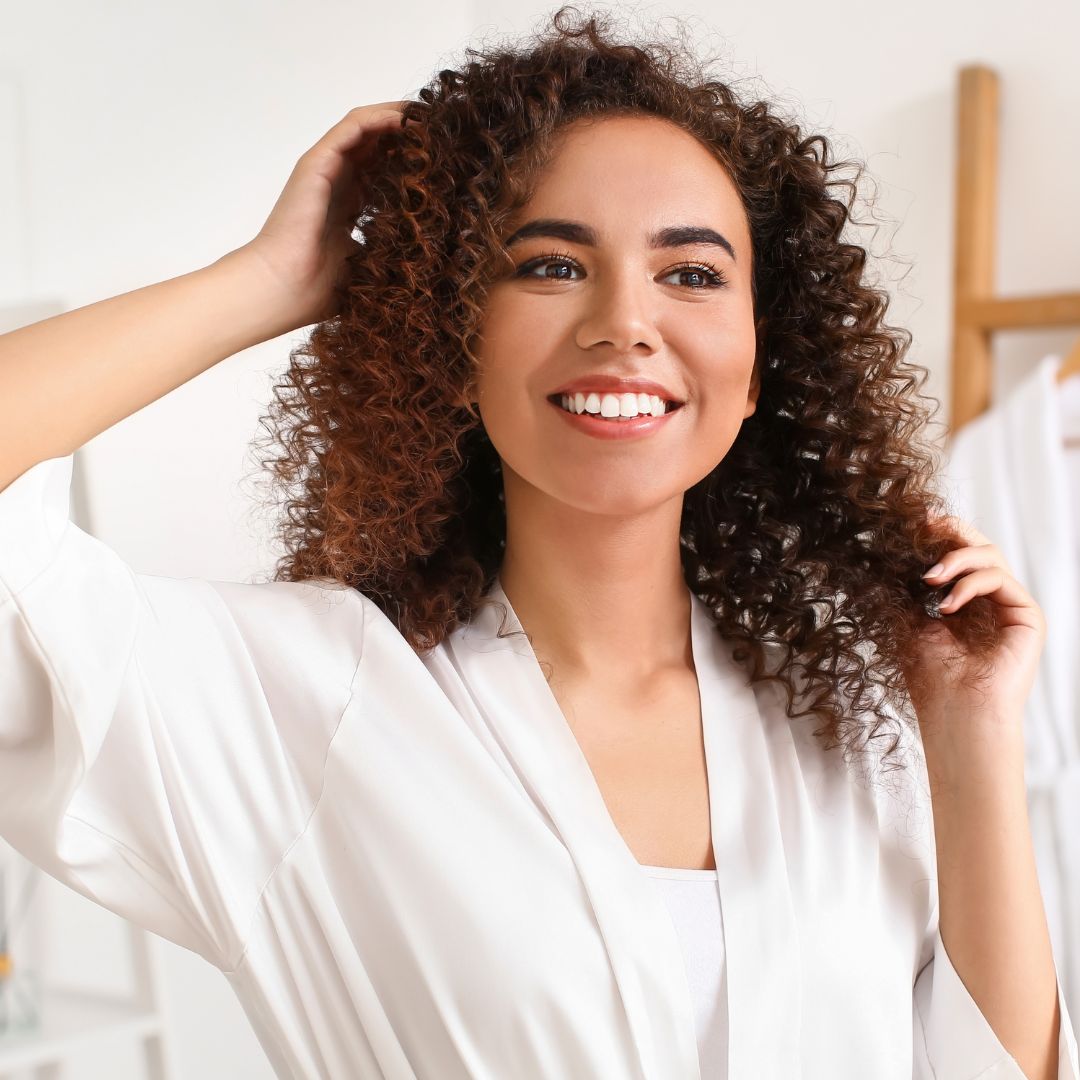 Woman in a bathrobe with curly hair touching her hair