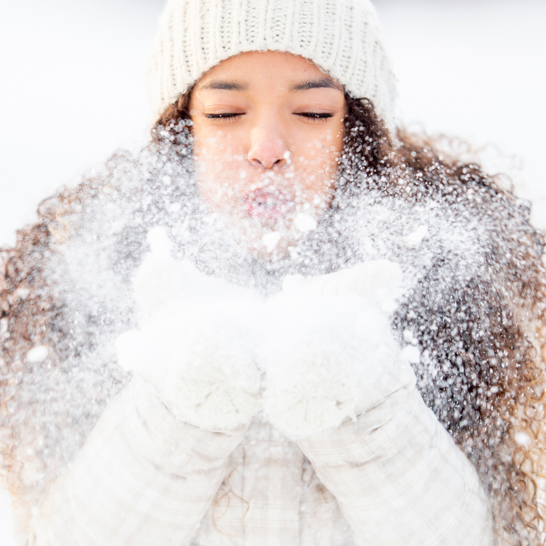 Woman holding snow into her hands and blowing it out of her hands.